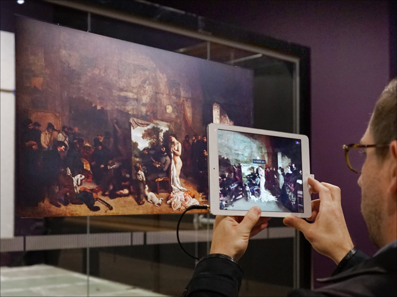 Visiteur tentant d'utiliser le dispositif de réalité augmentée réalisé par Orange pour informer les visiteurs sur le tableau "l'Atelier du peintre" de Gustave Courbet - Crédit: Flick Creative Commons / Jean-Pierre Dalbéra